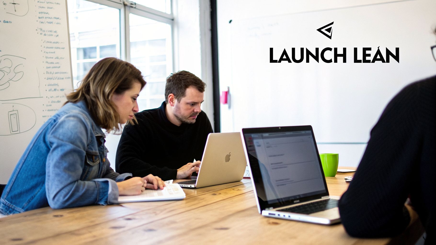 People collaborating in a modern coworking space, focused on laptops at a wooden table.