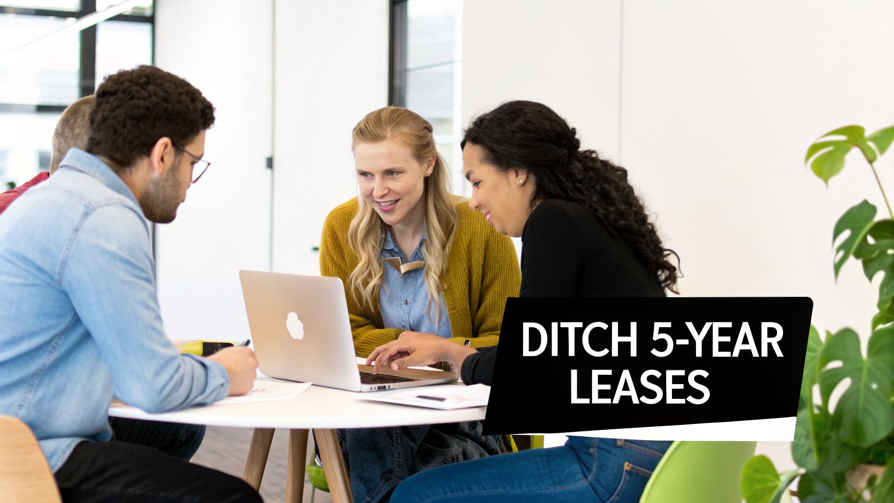 Four diverse people collaborating at a table with a laptop in a bright modern office.