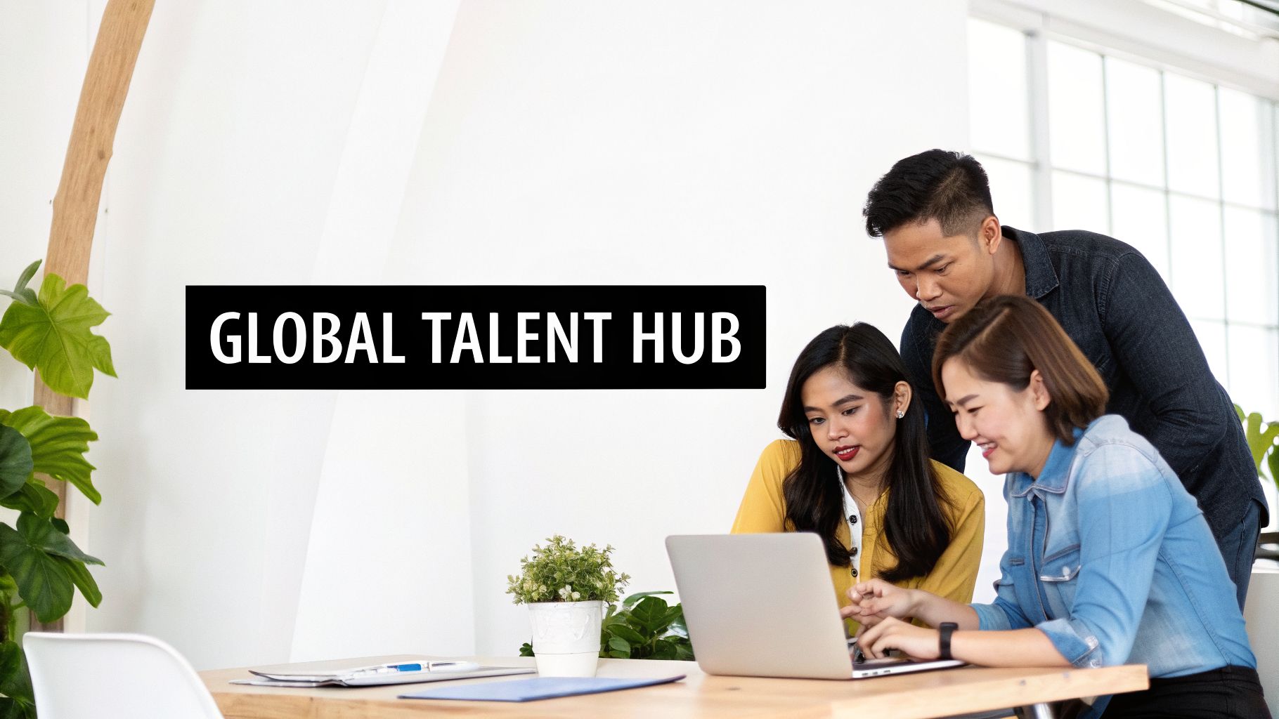 Three diverse professionals collaborate on a laptop in an office, discussing work under a 'GLOBAL TALENT HUB' banner.
