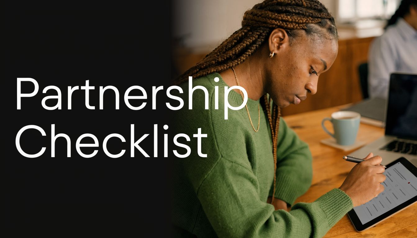 A woman in a green sweater writing on a digital tablet at a wooden desk.