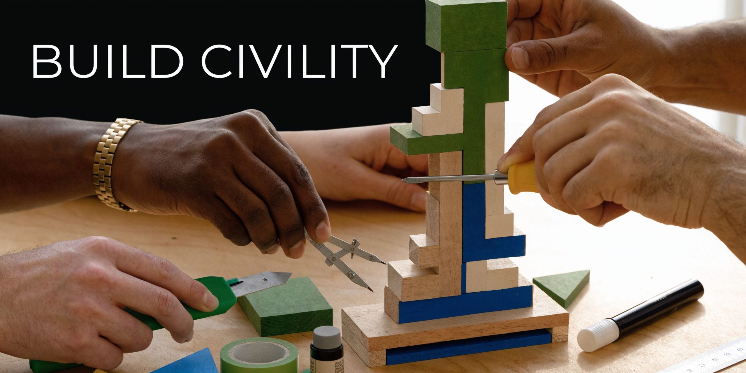 Multiple people using tools to construct a wooden block sculpture while working together at a desk.