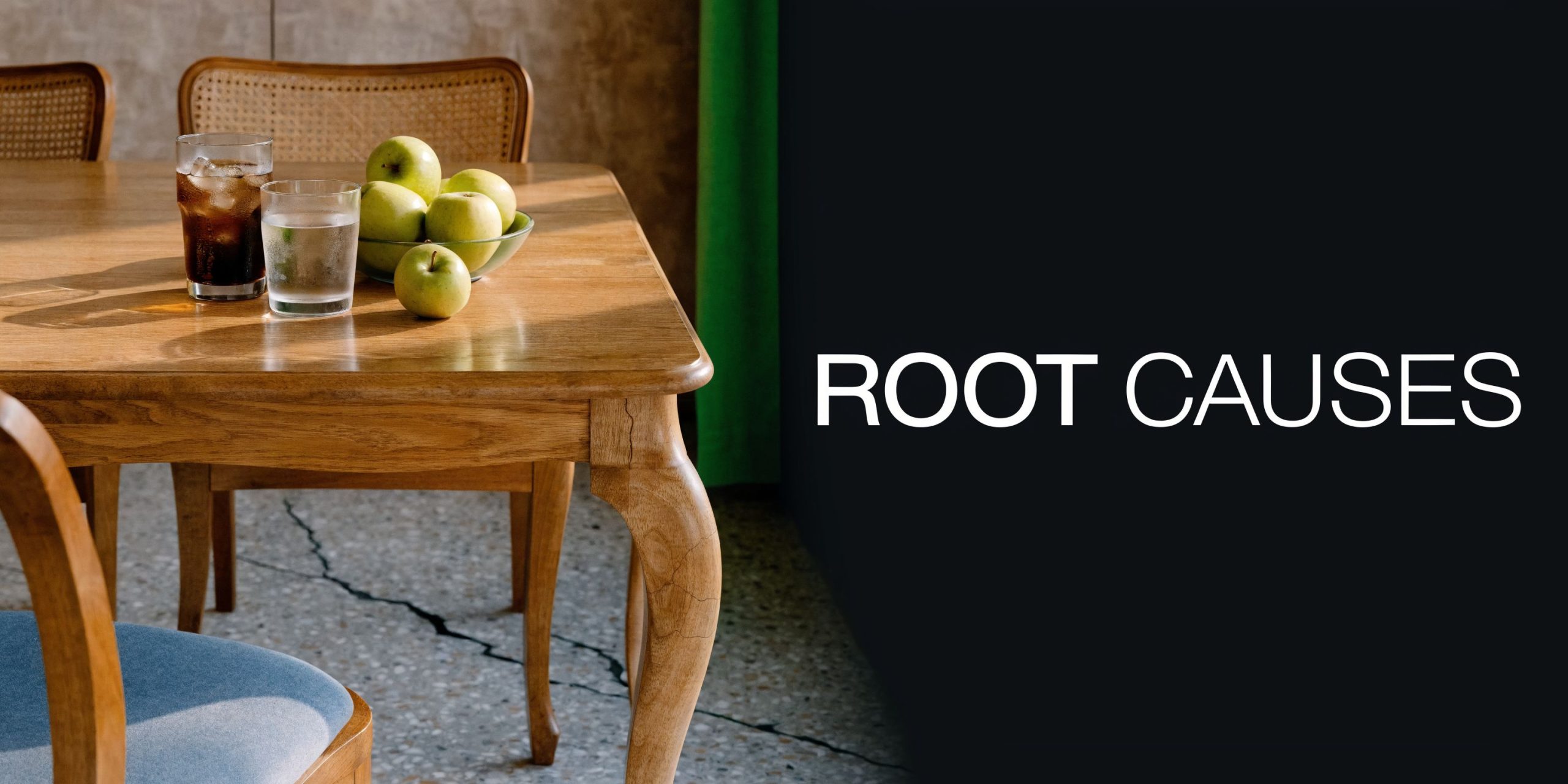 A wooden table set with drinks and fresh apples next to the words ROOT CAUSES written plainly.