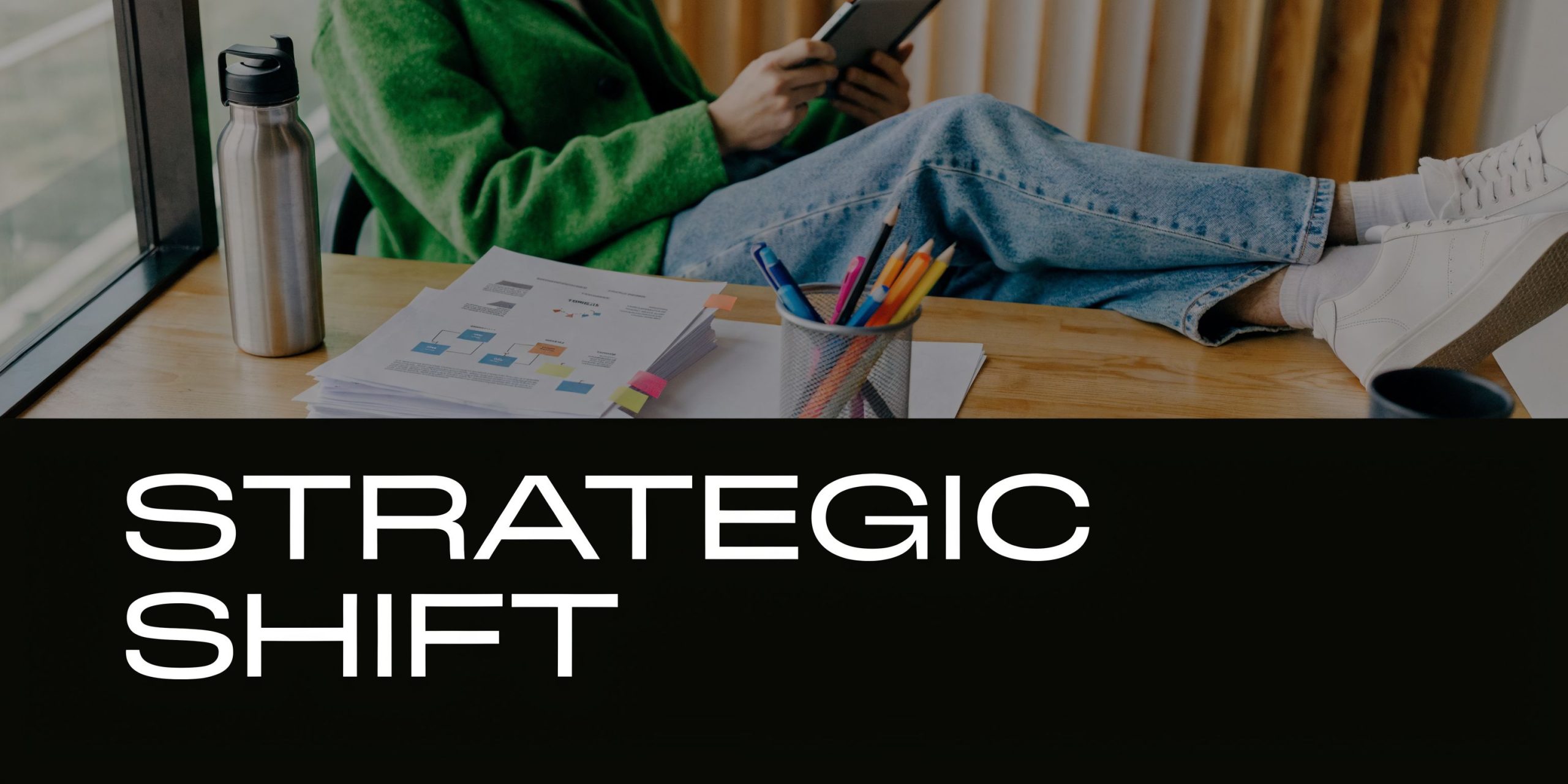 A person in a green sweater relaxing at a wooden desk with a tablet and business documents.